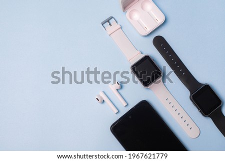 The layout of the watch and the phone on a blue background. Appliances and electronics. Modern gadgets. Phone headphones watch. Business. Student. Wireless headphone. Watch with pedometer. Copy space Royalty-Free Stock Photo #1967621779