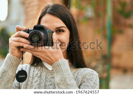 Young hispanic woman smiling happy using camera at the city.
