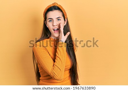 Young brunette teenager wearing casual yellow sweater hand on mouth telling secret rumor, whispering malicious talk conversation 