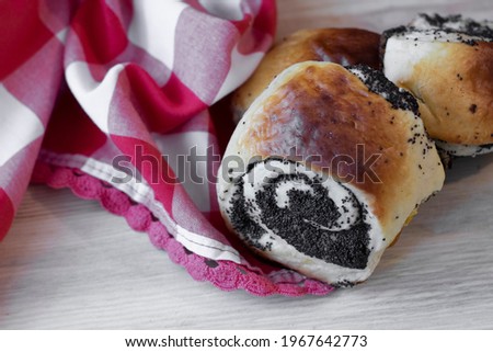 Three rolls with poppy seeds close-up on a wooden background with red and white cloth