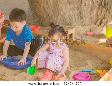 Asian boy and girl playing toy and sand in sandbox with natural background. Copy space.