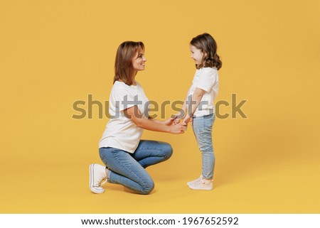 Full length happy woman in basic white t-shirt have fun with cute child baby girl 5-6 years old hold hands. Mom little kid daughter isolated on yellow color background studio. Mother's Day love family