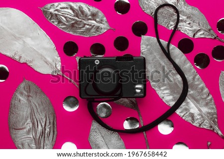 Vintage film camera on a pink background with silvery leaves and candy. Fashion photography concept.