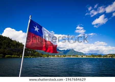 Villarrica lake, Chile in the summer. It is possible to see the lake, the flag of Chile. Sunny day, mountains in the background. Latin America, South America. Volcano, travel. Royalty-Free Stock Photo #1967684629