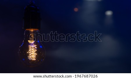 Close up of a glowing light bulb hanging in the dark copy space.