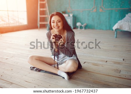 Indoor fashion portrait of pretty young brunette girl sitting on the floor and taking picture on vintage retro old school camera