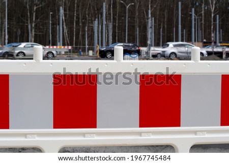 white and red plastic fence against the background of trees and moving cars during road repair