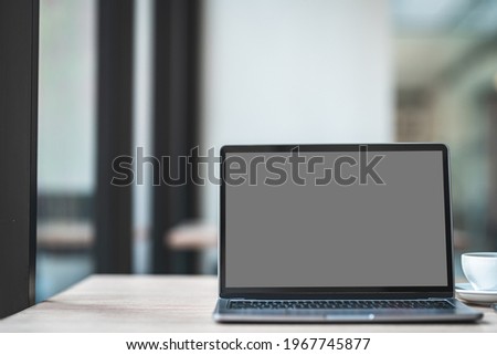 Mockup of laptop computer with empty screen with coffee cup and smartphone on table of the coffee shop background,Gray black screen
