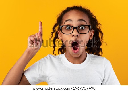 I Have Great Idea. Portrait of emotional African American girl in glasses pointing index finger up, thinking and finding inspiration or solution. Excited black kid with open mouth, studio wall, banner