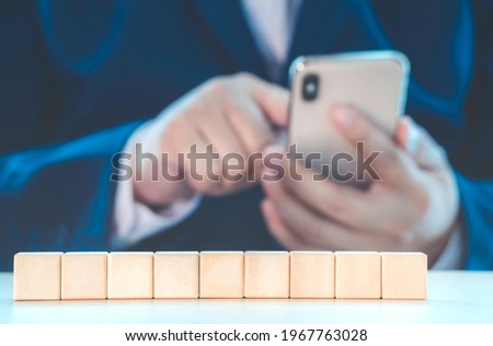Arranging empty wood cube in row amount 9 cubes against businessman using phone for information on table with copy space for input wording and infographic icon. Business growth and management concept.