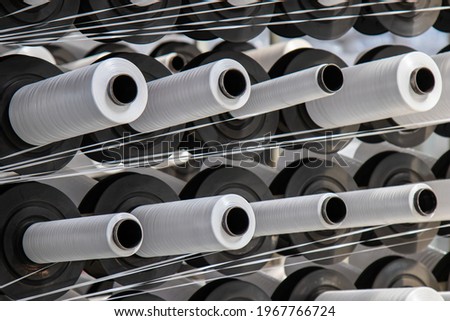 Coils of white flat polypropylene yarn for the production of industrial bags. circular loom woven bag machine. Production of polypropylene sleeves. Royalty-Free Stock Photo #1967766724