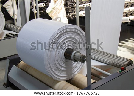 The resulting polypropylene sleeve for the manufacture of bags is wound on large reels. drum for winding sleeves of woven polypropylene yarns. PP bag production line Royalty-Free Stock Photo #1967766727