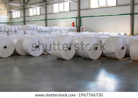 Raw materials warehouse. Many large coils of finished propylene hose made of woven thread for making industrial bags. Polypropylene rolls for packaging. Royalty-Free Stock Photo #1967766730