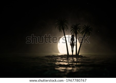 Romantic night scene. Fantasy night landscape with little island with palms and full moon over sea. Creative table decoration. Silhouette of a girl standing on little island. Selective focus.