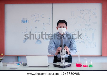 Science teacher wearingmask and   teaching with using microscope in the classroom