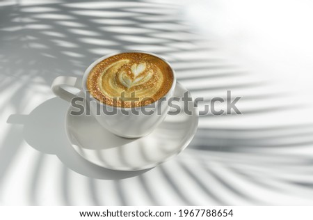 Latte art coffee on white background with palm leaves shadow. White on white and minimalist style.