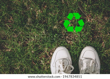 Recycling logo symbol in green.Concept of recycling the plastic, ecology, environmental conservation. Closeup top view of legs, white sneakers.Shoes walking on grass.Copyspace for text, flatly, banner Royalty-Free Stock Photo #1967834851