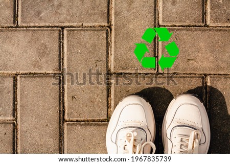 Recycling logo symbol in green.Concept of recycling the plastic, ecology, environmental conservation. Closeup top view of legs, white sneakers.Shoes on paving slabs. Copyspace for text, flatly, banner Royalty-Free Stock Photo #1967835739