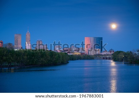 A super moon rises over the Indianapolis, Indiana skyline as the buildings reflect the pink glow of the sunset. 