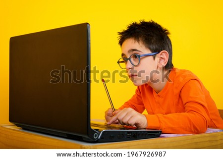 Child hears a remote lesson with the school teacher due to covid-19 pandemic. yellow background Royalty-Free Stock Photo #1967926987