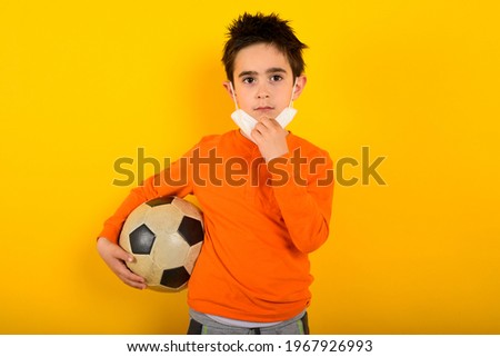 Child wants with face mask for covid-19 coronavirus wants to play at soccer. yellow background