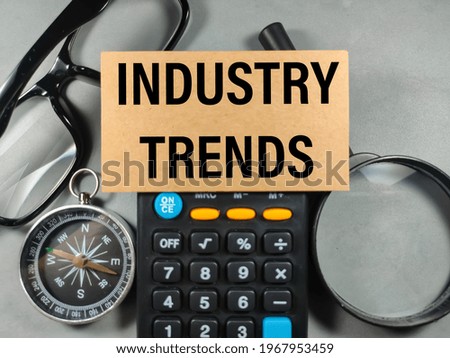 Business concept.Text INDUSTRY TRENDS with calculator,compass,glasses, and magnifying glass on gray background.