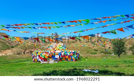 A big white heap of stones (aobao) with panoramic view on Daqing mountains in Inner Mongolia. It has a few colorful prayer flags attached to it and waving around it. Desolated landscape. Spirituality Royalty-Free Stock Photo #1968022291