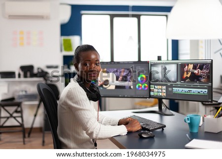 Black videographer smiling at camera editing video project in post production software working in creative studio office. African movie maker editing audio film montage on professional computer