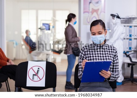 Stomatology patient in denstiry wainting area filling form before consultation with dentist dressed in ppe suit as safety precation agasint infection with coronavirus ,during global outbreak.