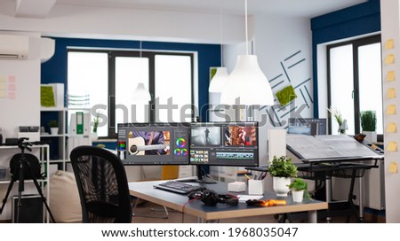 Empty modern creative agency office with dual monitors setup with processing video film montage. Video editing start up studio company with no people in it and post production software on pc displays