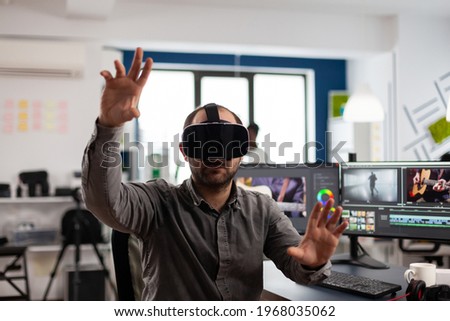 Video editor experiencing virtual reality headset, gesturing, editing film montage using post production software working in creative agency office. Videographer using VR goggles in multimedia company