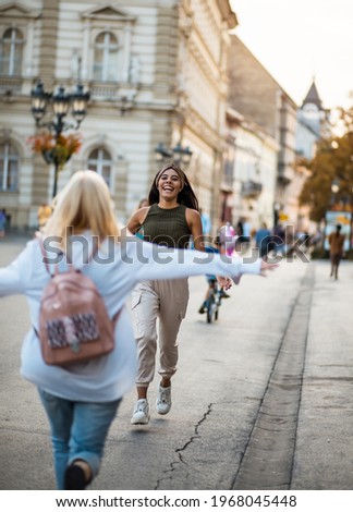 Two women on the street. They run into each other's arms.