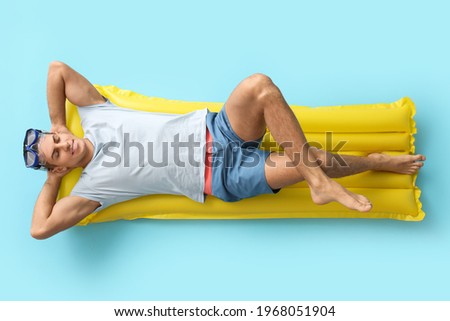 Young man lying on inflatable mattress against color background