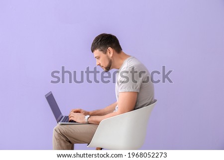 Man with bad posture using laptop while sitting on chair against color background Royalty-Free Stock Photo #1968052273