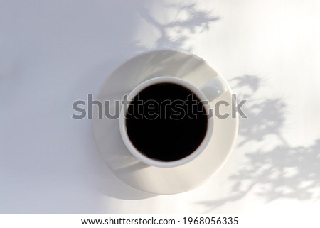 Cup of coffee and plant shadow on white table background. Spring or summer flat lay minimalist still life. Top view, copy space. Summer vacation good morning concept