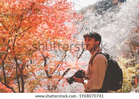 Asian Traveler taking a photo of Gorgeous fall foliage of red maple leaves on Autumn season against a backdrop of Shikizakura Four-Season Cherry Blossom Trees at Obara, Toyota-City Aichi, Japan.