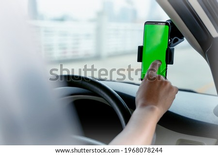 Mock up of man using mobile smart phone inside a car. Driver hand holding blank green screen smartphone, searching address and pin location via map navigator application, transportation technology