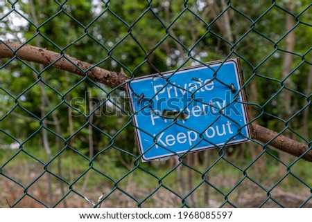 A blue and white sign on a mesh wire fence which states private property keep out 