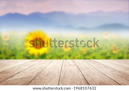 Wooden table top with blurry Sunflower field against mountains landscape 