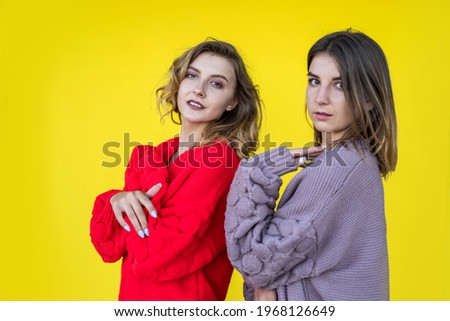 Fashion girlfriends wear modern knitted sweater posing on yellow wall as background.