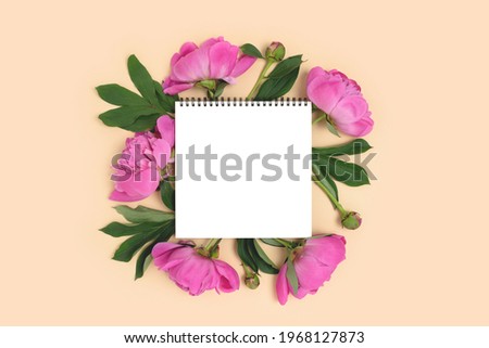 Notepad mockup with wreath made of peony flowers on a beige background. Creative template with copy space.
