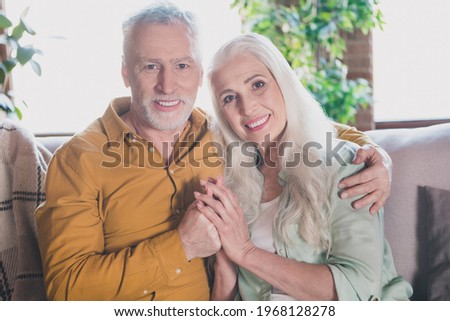 Photo of charming cheerful old people hug hold hands family smile sit sofa indoors inside house home apartment