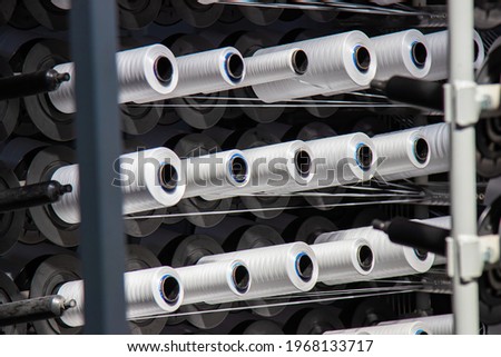 Coils of white flat polypropylene yarn for the production of industrial bags. circular loom woven bag machine. Production of polypropylene sleeves. Selective focus. Royalty-Free Stock Photo #1968133717
