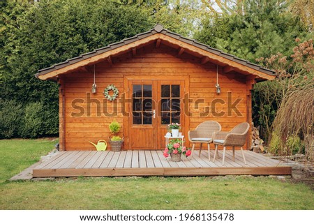 Small wooden hut in the garden. Garden shed with a chair in front of the door. Nice wooden hut in the countryside in a small forest  Royalty-Free Stock Photo #1968135478