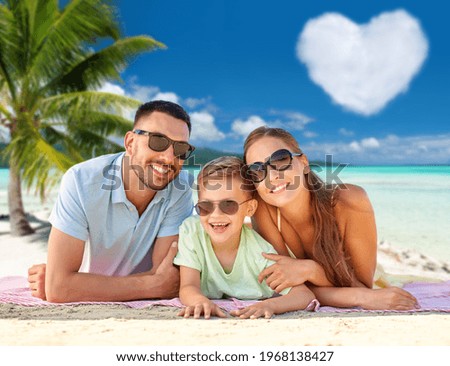 family, travel and tourism concept - happy mother, father and little son in sunglasses lying on blanket over tropical beach in french polynesia and heart shaped cloud on background