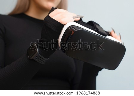 Young woman holding VR glasses in her hands, close-up. Girl using interactive device, indoors. New technologies, simulation equipment concept. Selective focus on virtual reality glasses.