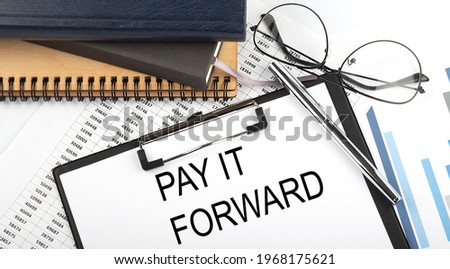 Text PAY IT FORWARD on Office desk table with notebooks, supplies,analysis chart, on white background. Top view