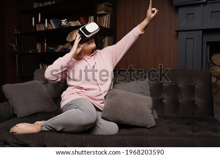 Casual caucasian girl using VR headset at home in pink hoodie and grey pants.
