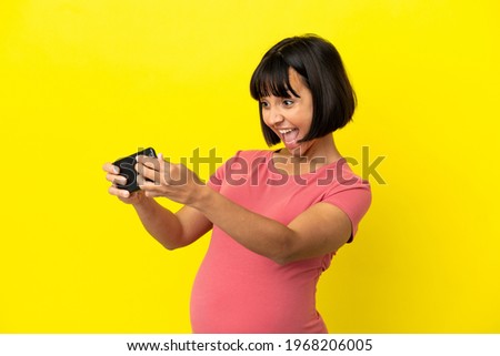 Young mixed race pregnant woman isolated on yellow background playing with the mobile phone