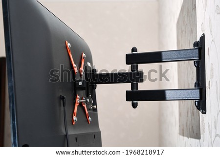 Swivel TV bracket LED display. Back view. X-shaped red fasteners. Black color. Multiplanar. Hangs on a wall. Reliable and comfortable fastening. Childproof and rollover protection. Metallic equipment. Royalty-Free Stock Photo #1968218917